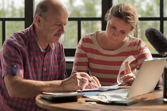 daughter helps her father count money and manage the family budget. Senior man looking on bills and taxes. Symbolbild: Vater und Tochter am Budgetieren