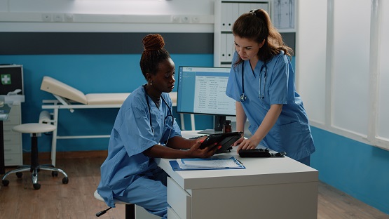 Medical team working with digital tablet for healthcare system in doctors office. Healthcare assistants talking while looking at display for examination and treatment. Nurses in cabinet Symbolbild: 2 Arzthelferinnen