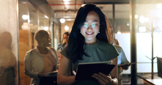Night, tablet and business people walking in office after finishing work task. Tech, overtime and Asian woman with group of friends going home after working late on sales project in dark workplace. Symbolbild: Frau mit Tablet